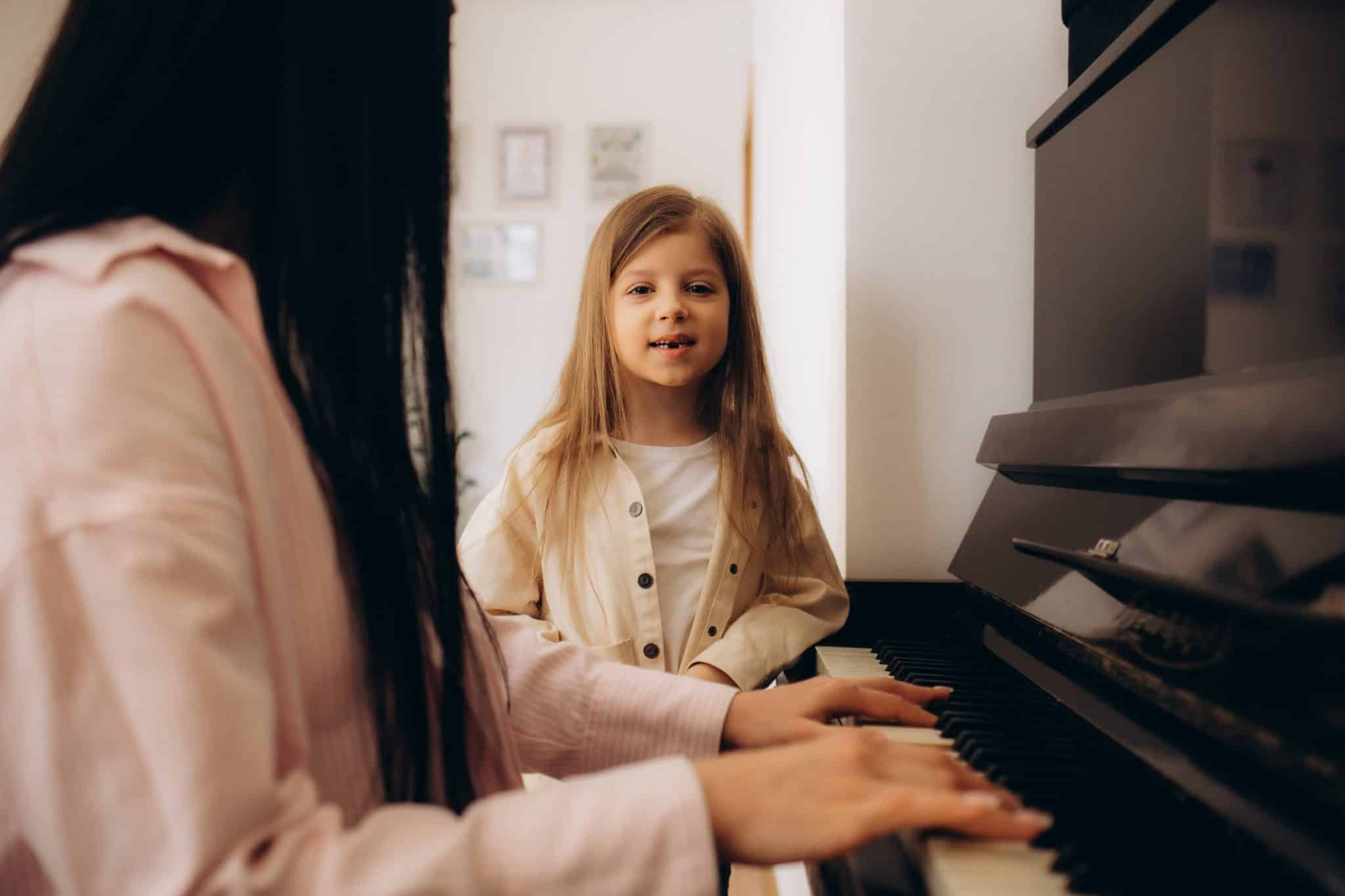 Small girl learning play piano with teacher