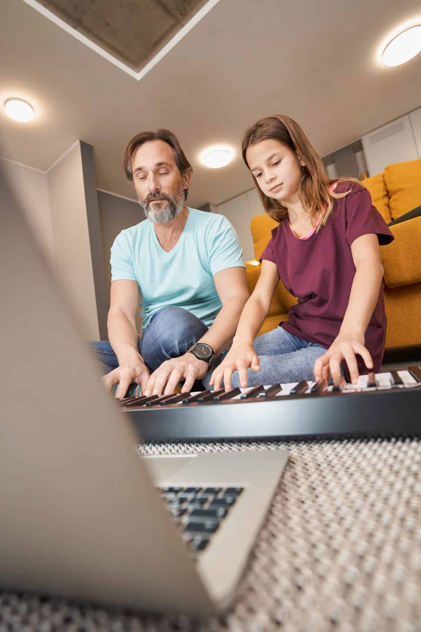 Adult male with teenager playing synthesizer on living room floor