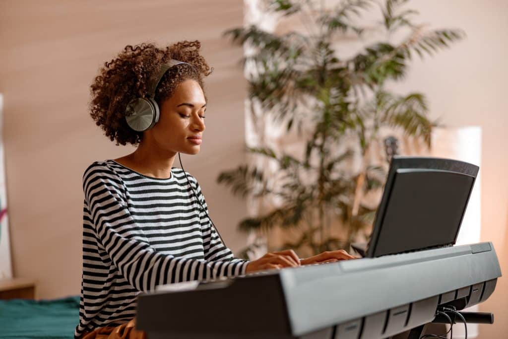 Young female musician playing melody on electronic musical instrument while spending time at home