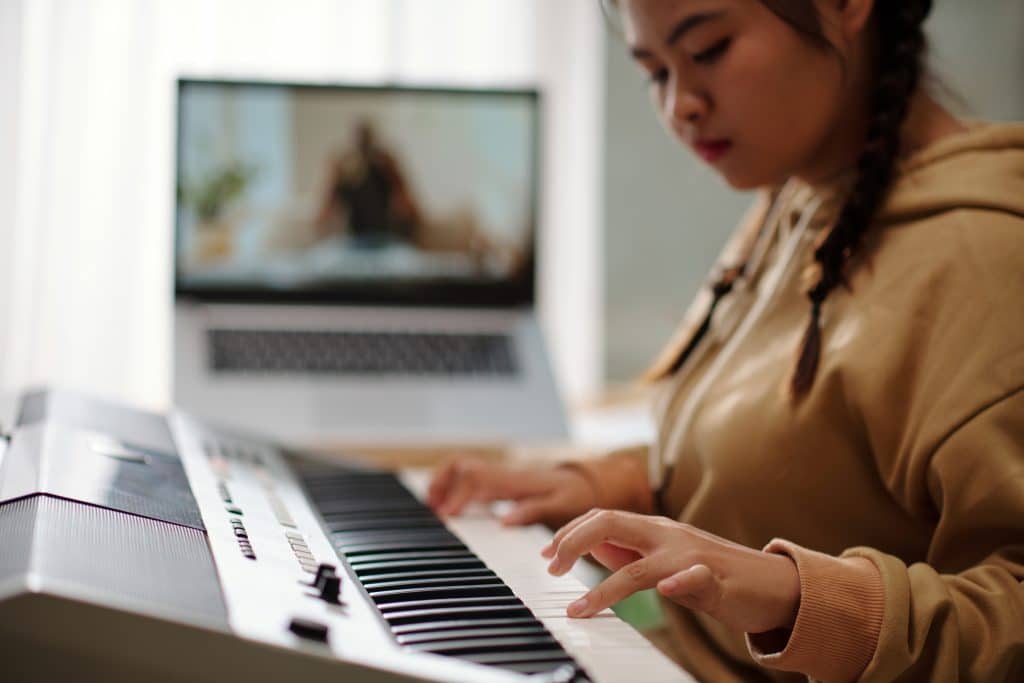 Girl playing synthesizer at home after online class with music teacher