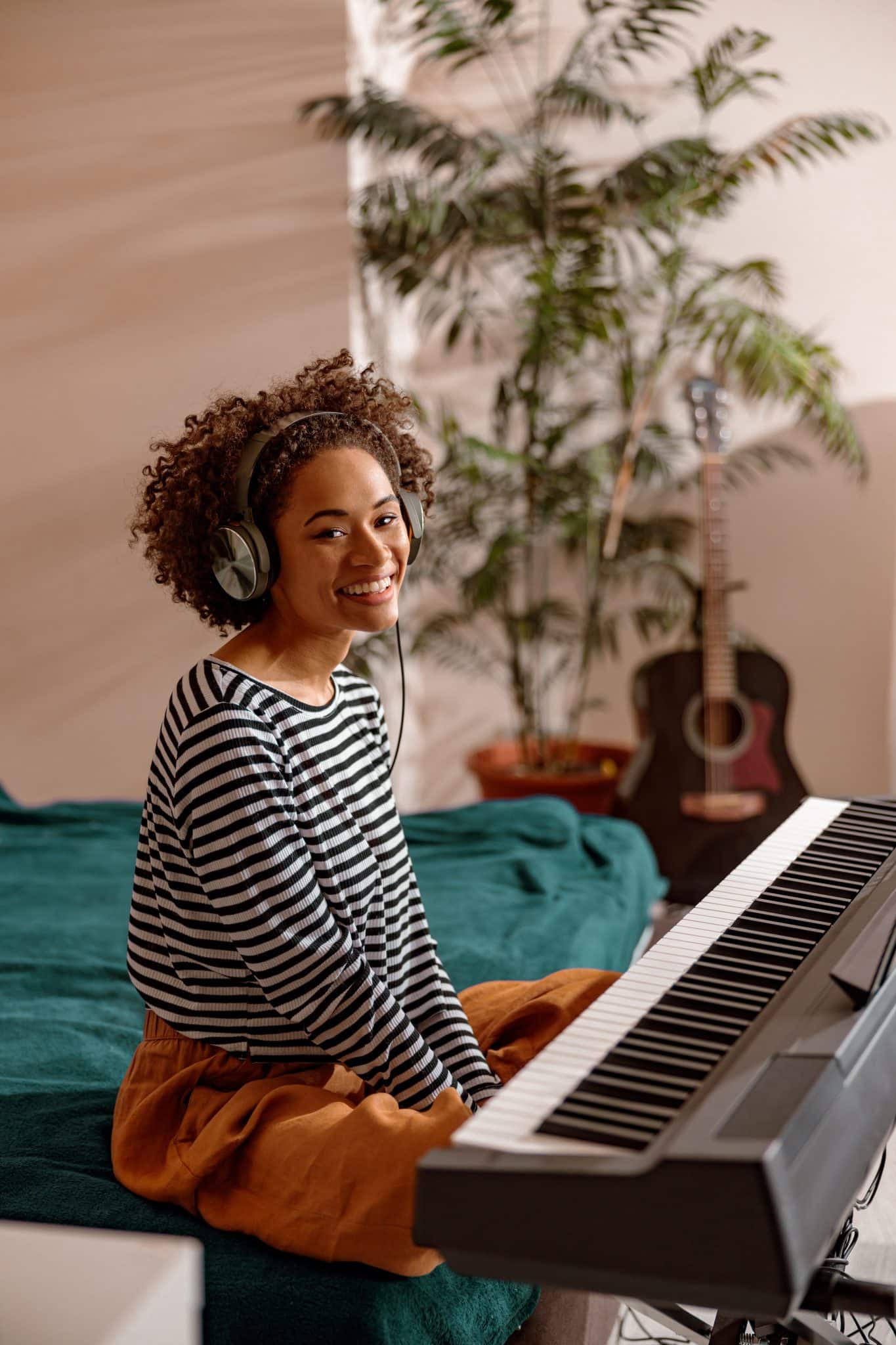 Joyful woman in headphones sitting near synthesizer at home