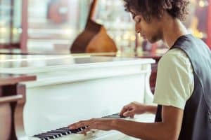 Handsome Afro-American man in classical vest playing a piano in a musical shop