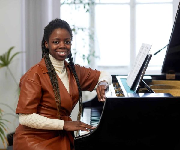 Portrait of African young woman smiling at camera while sitting at the piano and learning the notes